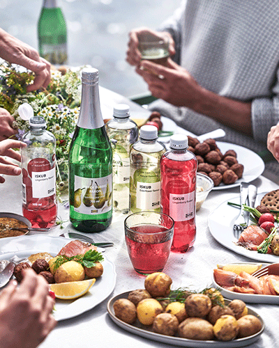 A table full of food, with several plates of Swedish meatballs, potatoes, salmon, and beverages. People are eating, some are out of focus in the background.
