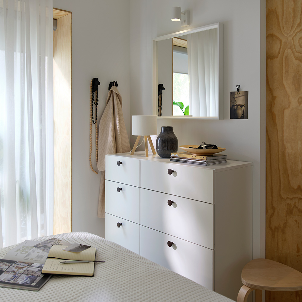 A bedroom setup with LASTARE chest of drawers placed below a wall mirror and decorated with various items