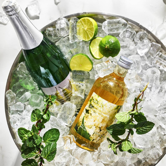 Beverage concentrate bottles with lime, mint, and ice in a metal bucket filled with ice.