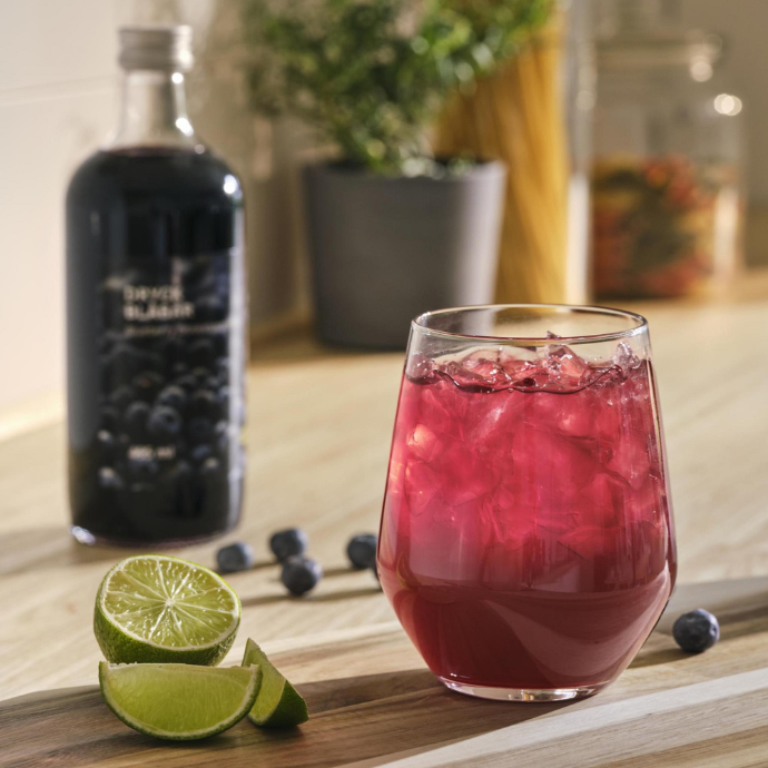 Frozen tea Glass of pink iced drink on a wooden board with a blueberry drink concentrate bottle, limes, and fresh blueberries.cubes with milk