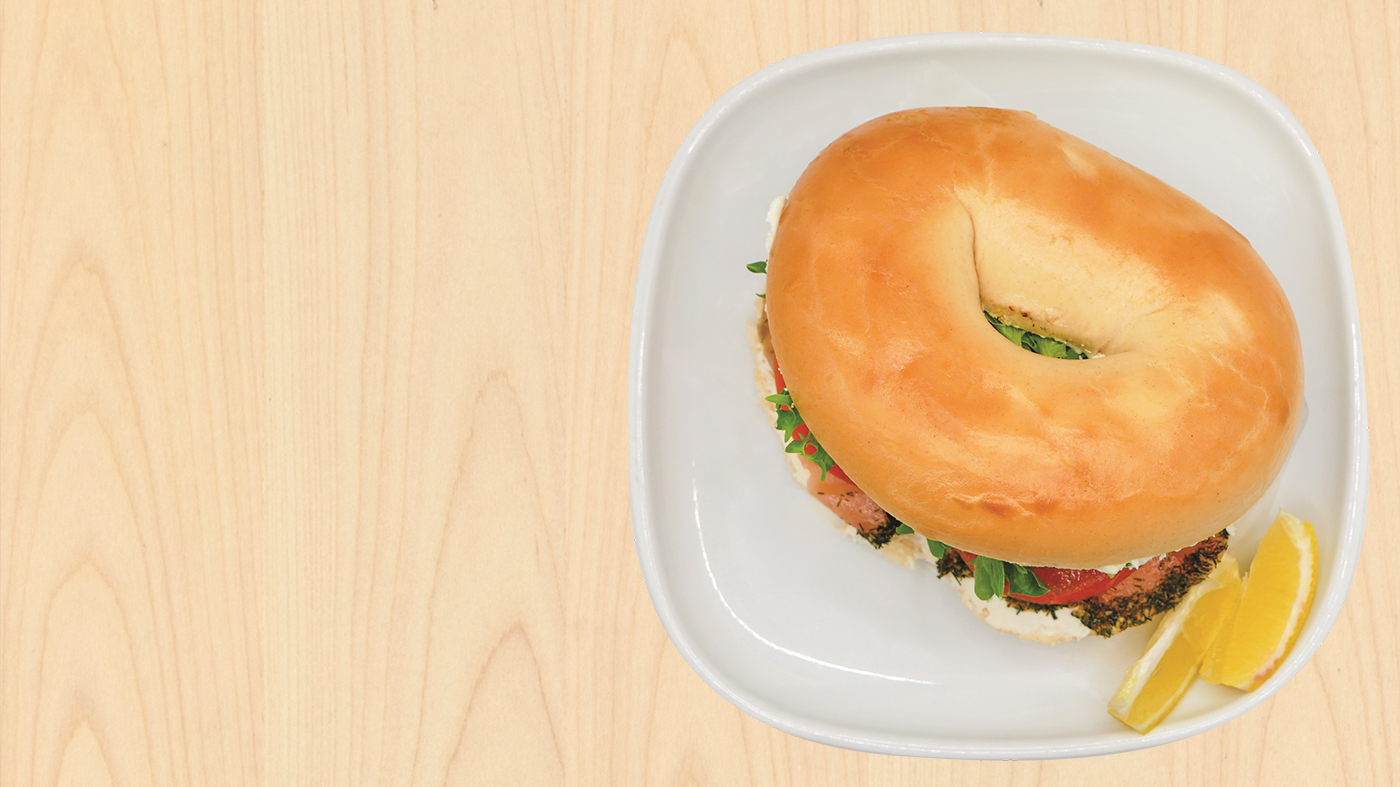 Bagel sandwich filled with salmon and vegetables, served with lemon slices.