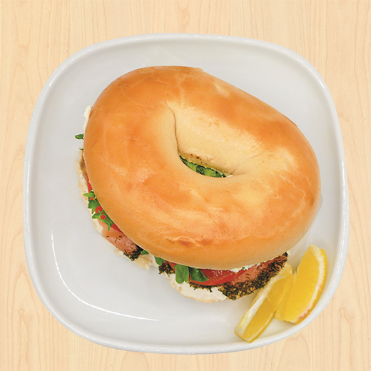 Bagel sandwich filled with salmon and vegetables, served with lemon slices.