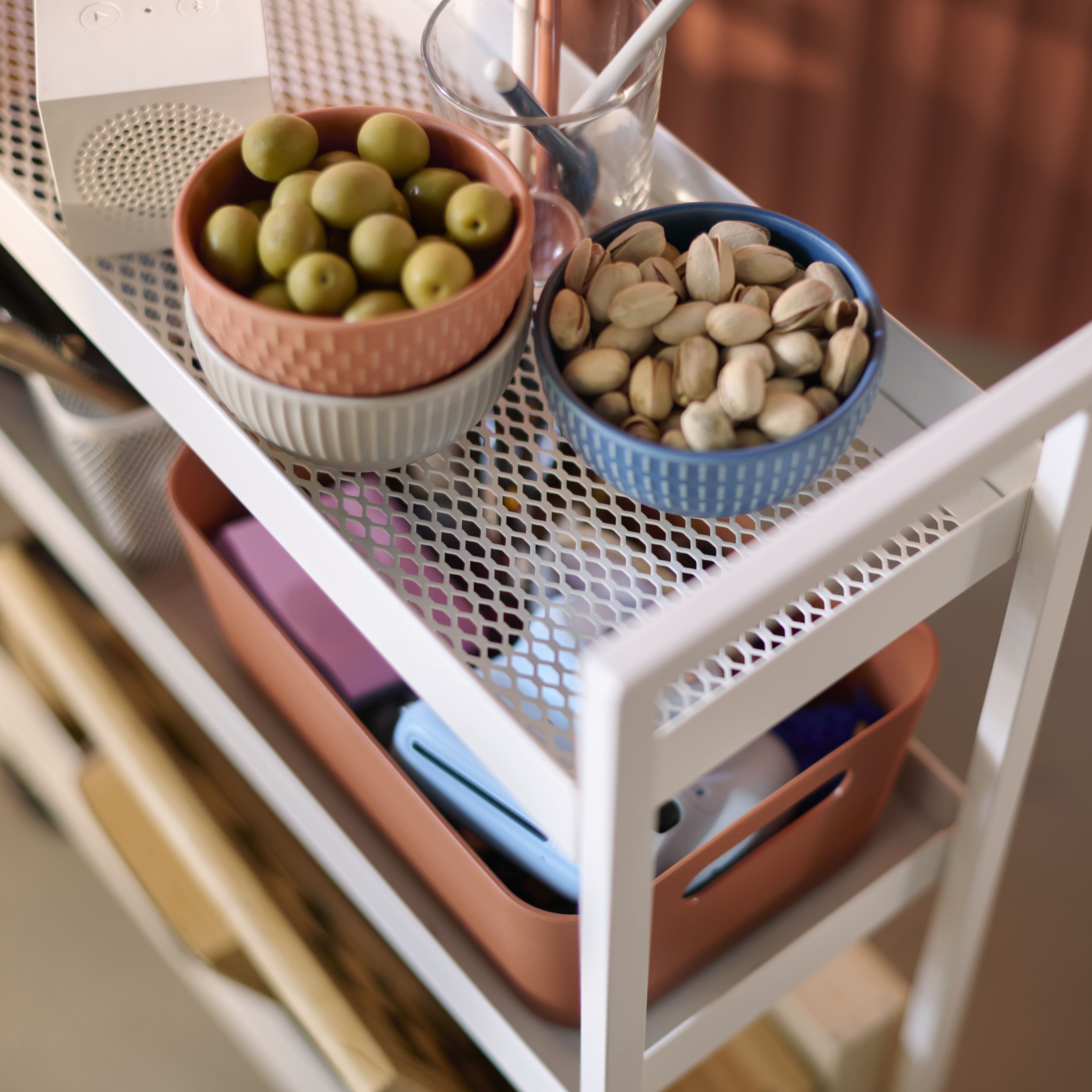 Top view of a white cart with bowls of olives and pistachios, and an orange organizer below.