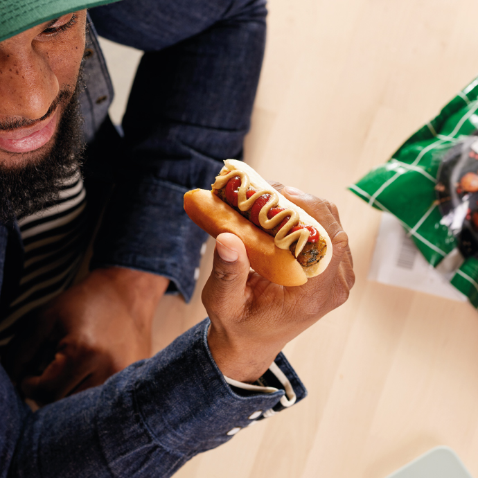 Hombre sosteniendo un hot dog con ketchup y mostaza listo para comer.