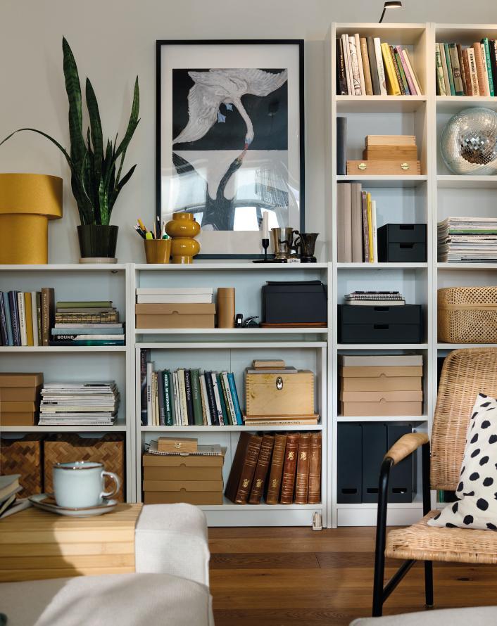 White shelving unit with books, storage boxes, and decor, including a plant and a gold lamp.