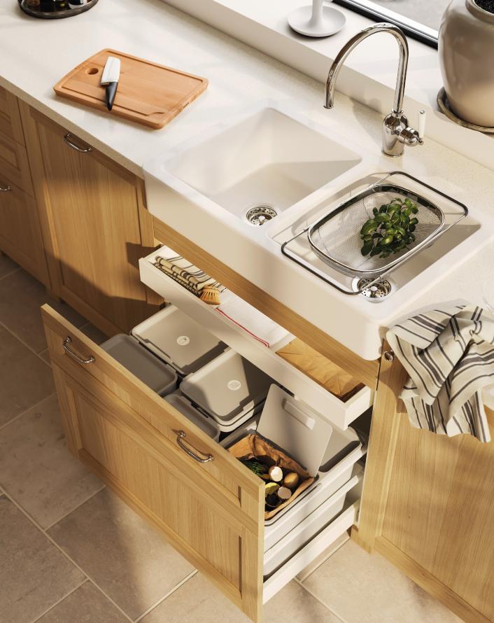 Kitchen sink with wooden cabinet and open drawers showing organized recycling containers.