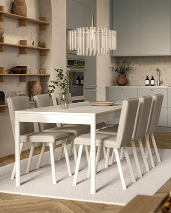 Comedor moderno con mesa blanca, sillas tapizadas en beige y una lámpara de cristal elegante sobre una alfombra clara.