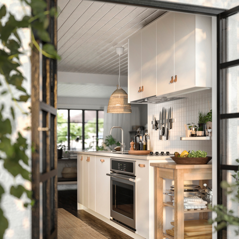 Modern white kitchen with wood accents, a wicker pendant light, and a stainless steel oven viewed through a doorway.