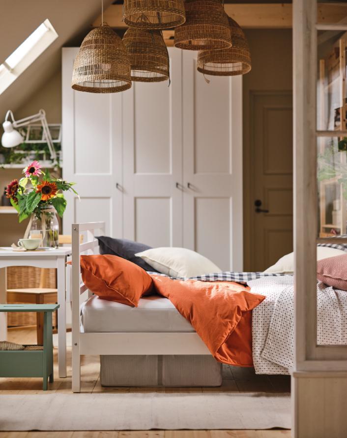 A bright bedroom featuring a bed with orange bedding, woven pendant lamps, and a large white wardrobe in the background.