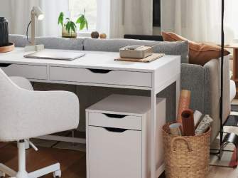 Un escritorio blanco con cajones ubicado detrás de un sofá gris, que incluye una silla blanca y una cajonera a juego.