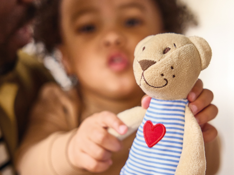 Young child holding a teddy bear with a red heart in a sweet and intimate moment.
