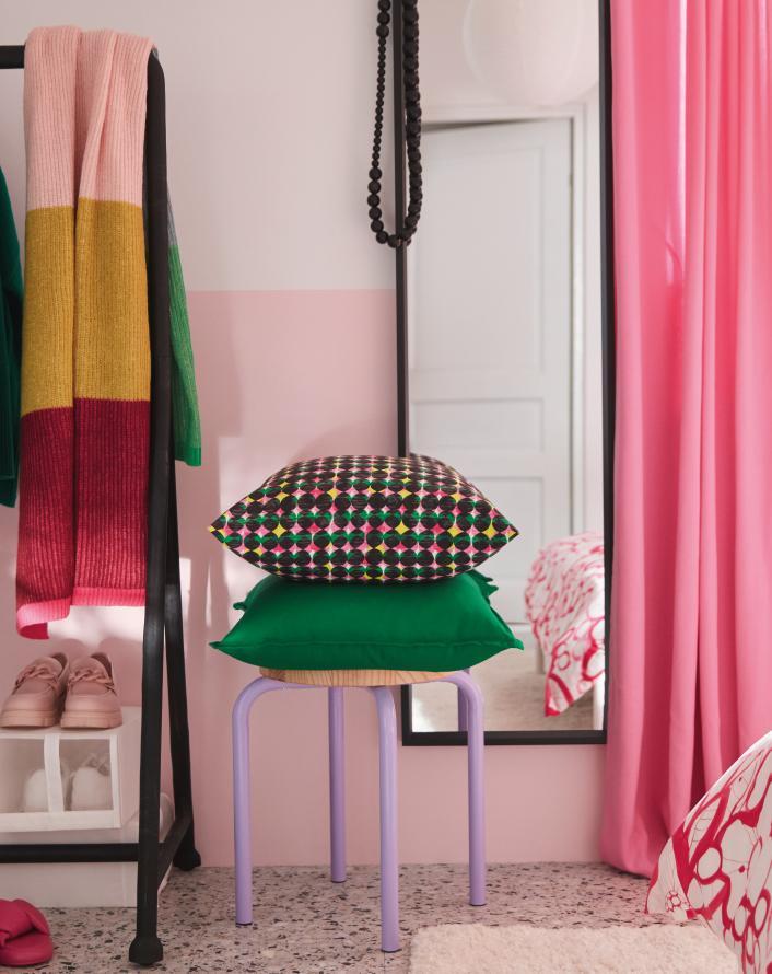 Bedroom corner with colorful cushions on a chair, clothing rack, mirror, and pink curtains.
