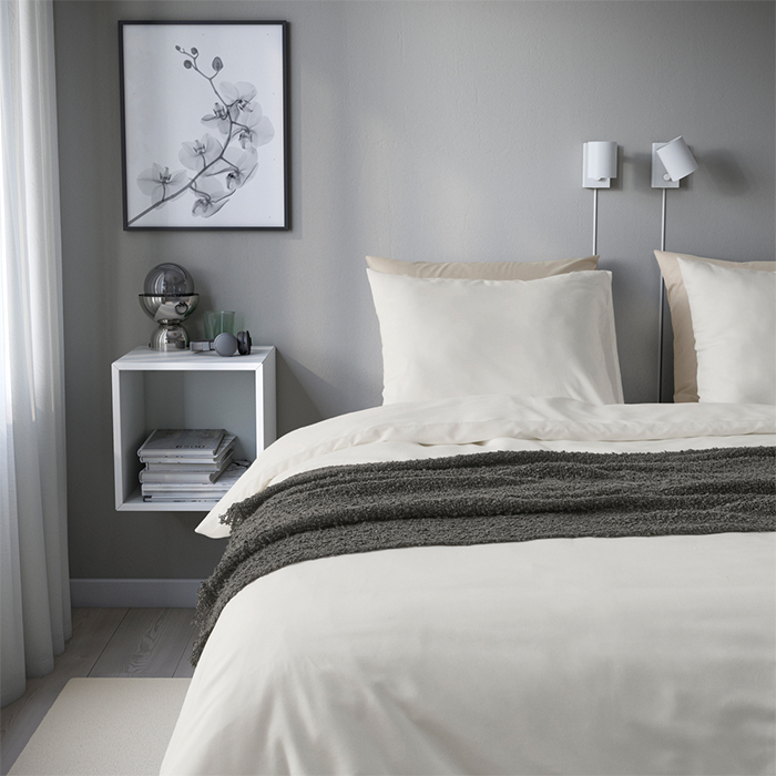 Una cama nido de madera clara situada junto a una ventana grande que da a un bosque, decorada con cojines de rayas y una manta con flecos.