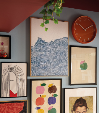 Composición de cuadros enmarcados con ilustraciones artísticas y reloj redondo naranja sobre pared gris, en una decoración de estilo moderno y creativo.