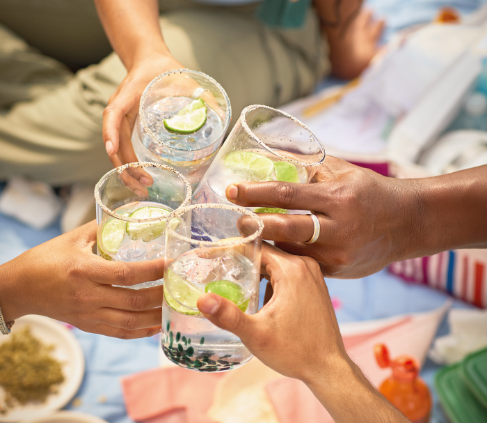 Grupo de personas brindando con vasos de bebida con hielo y rodajas de lima, en un ambiente informal y festivo.