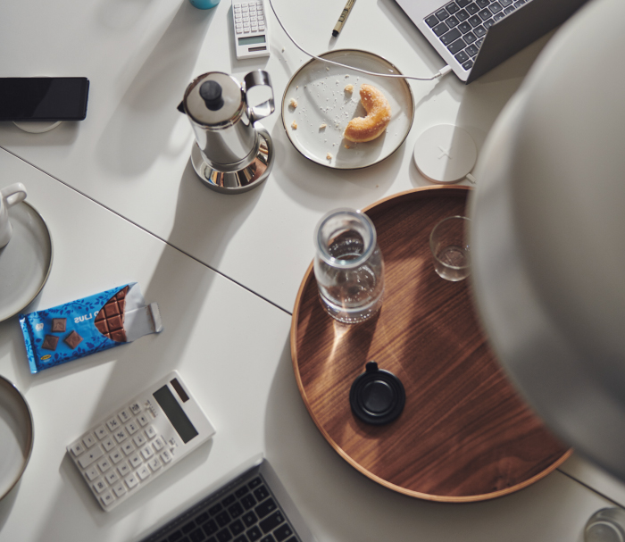 Vista cenital de un escritorio con laptops, calculadoras, café, chocolate y una rosquilla a medio comer.