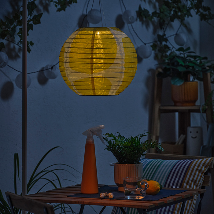 SOLVINDEN solar lamp next to a TÄRNÖ table and chair set, with a HONUNGSPALM plant pot on top. Additionally, a KORALLBUSKE cushion on top.