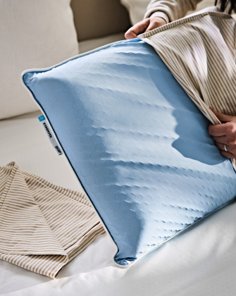 Hand holding a blue pillow with a partially removed cover.
