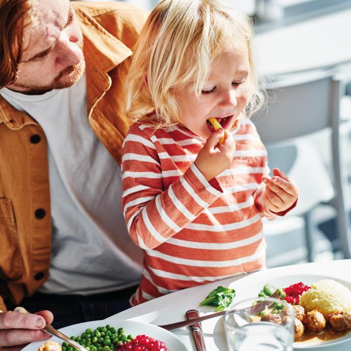 Una persona adulta y un niño compartiendo una comida, mientras el niño come en la mesa del comedor.
