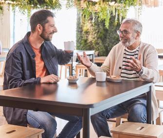 Dos personas sentadas en una mesa de cafetería, disfrutando de un café y manteniendo una conversación amistosa.