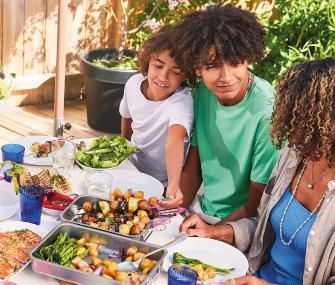 Personas sirviendo verduras asadas en una comida al aire libre.