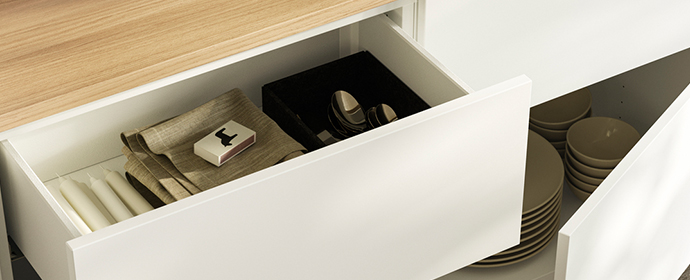 Close-up of a white dresser with open drawers, candles, and silverware inside