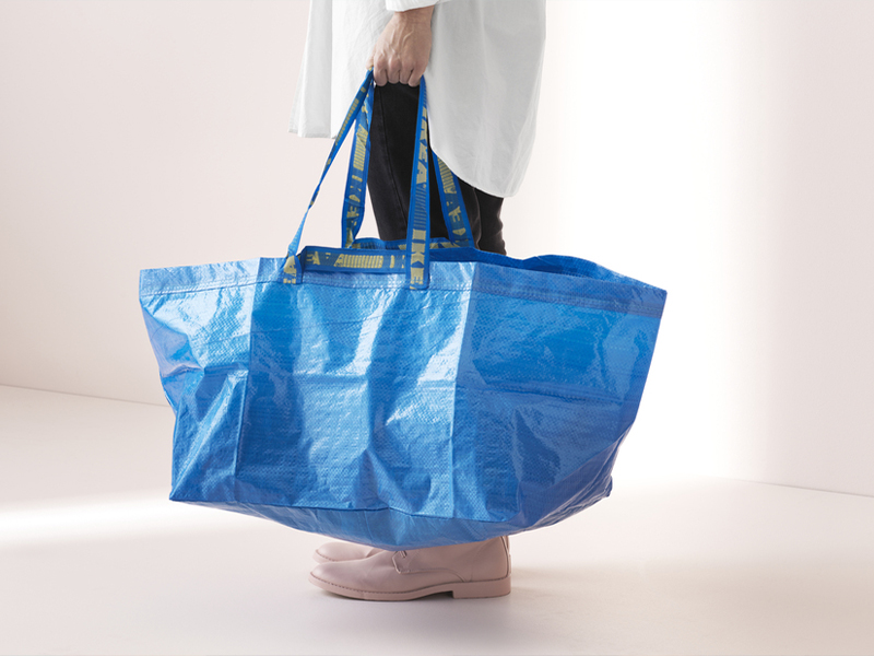 Person holding a large blue shopping bag with yellow straps against a neutral background.