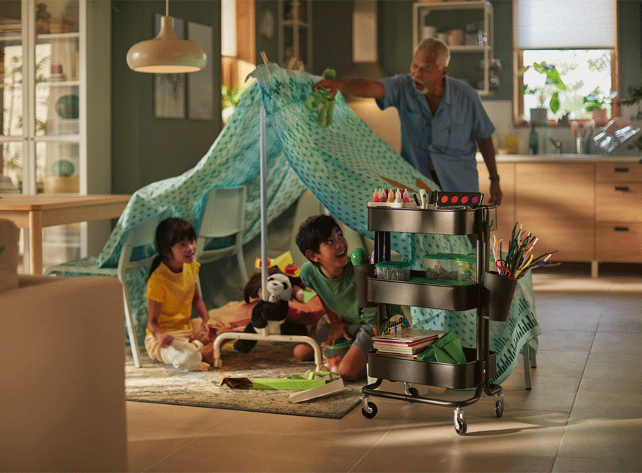 Grandfather and grandchildren playing inside a homemade blanket fort in the living room.