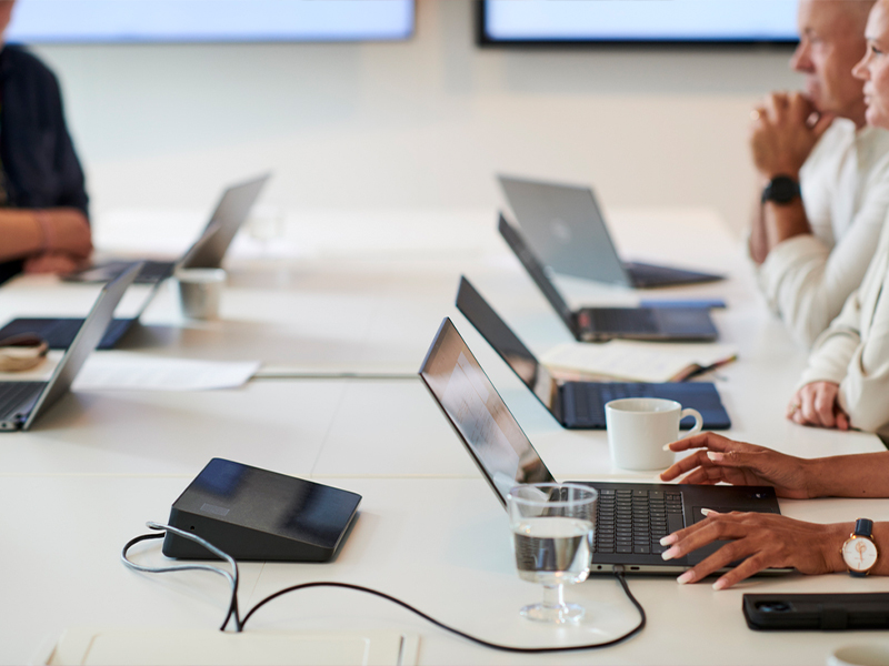 People gathered around a conference table with multiple open laptops during a meeting.