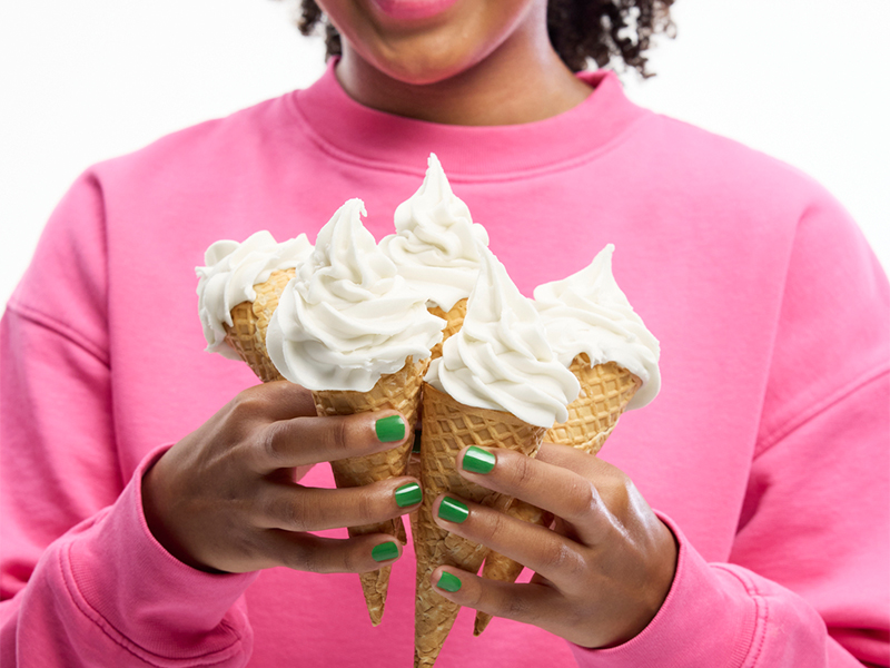 Person in a pink sweatshirt holding a bouquet of four vanilla ice cream cones.