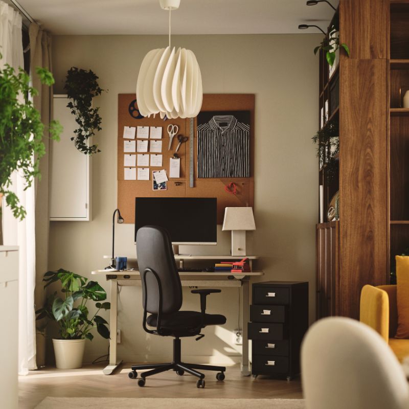 An office with a dark grey SMÖRKULL office chair with armrests beside a desk and plants near a wall.
