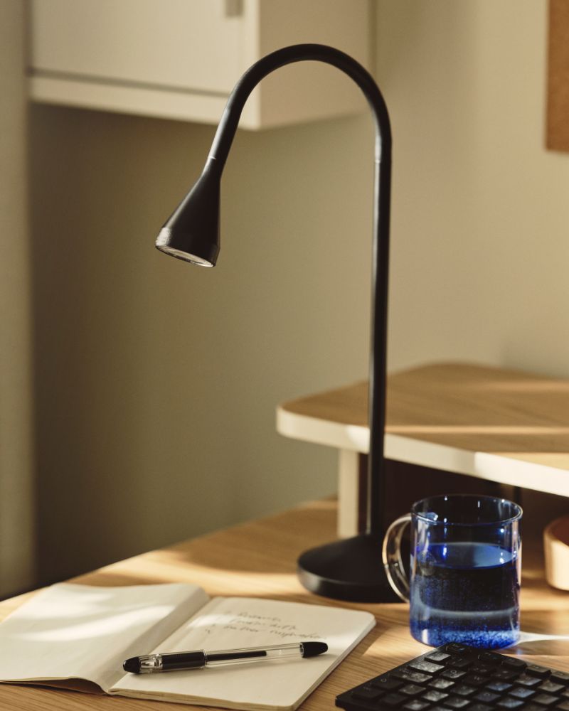 Close-up of a NÄVLINGE work lamp with a notebook and pen.