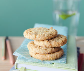Tres galletas apiladas sobre cuadernos pastel con un vaso al fondo.