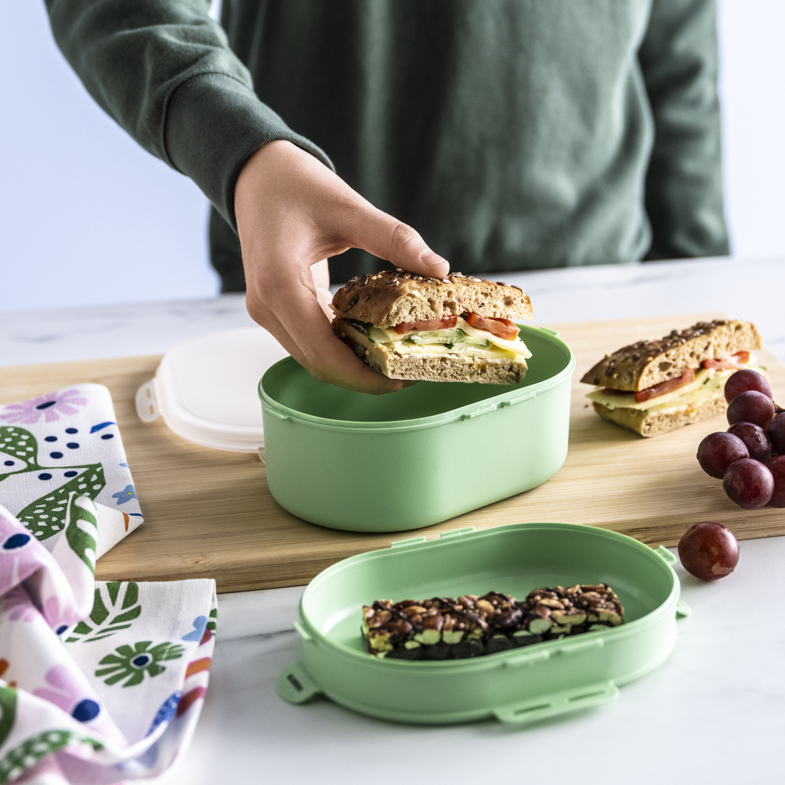 Lonchera verde con sándwich, barra de cereal y uvas.