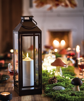 Farol negro con vela encendida sobre una mesa decorada con elementos naturales.