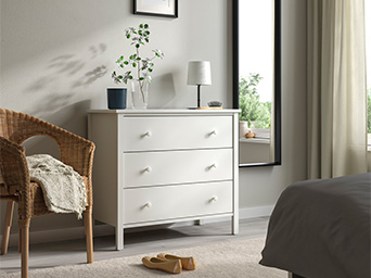 Dormitorio acogedor con cómoda blanca, espejo de cuerpo entero y sillón de mimbre.