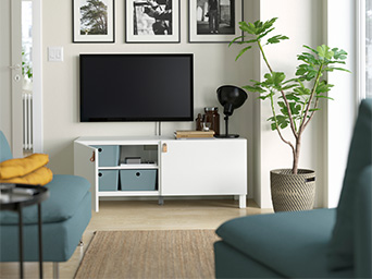 Sala de estar con mueble para TV blanco, cuadros en la pared y planta en maceta.