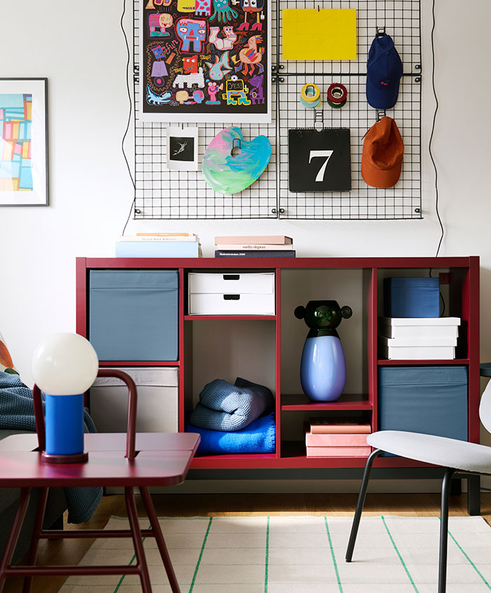 En el salón hay una estantería KALLAX de color marrón rojizo y negro con compartimentos, colocada junto a una pared decorada.