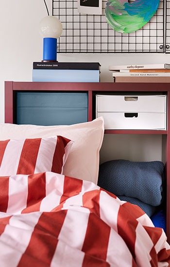 Un dormitorio con una caja azul de DRÕNA colocada sobre una estantería roja.