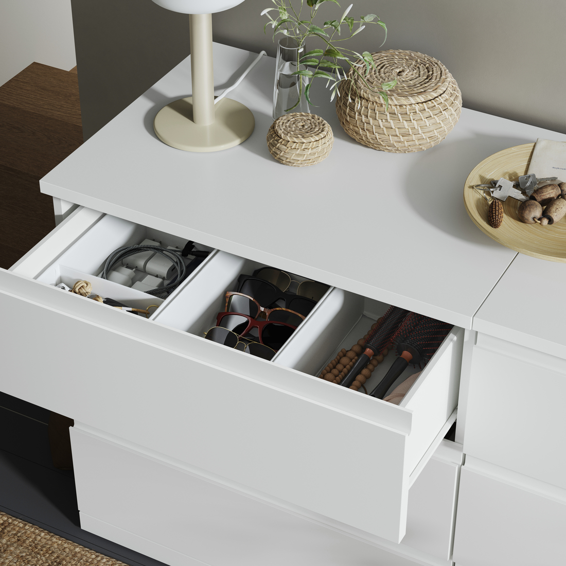 lose-up of an open white dresser drawer neatly organized with dividers holding cords, sunglasses, and hairbrushes.